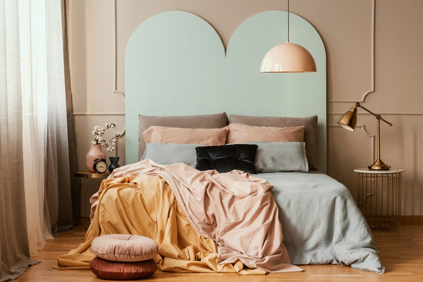 Bedroom with brown painted walls, blue headboard, pastel colored pillows, comforter and brass lamps