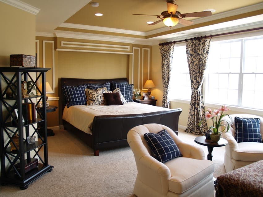 Bedroom with ceiling fan, freestanding shelves, white chairs, windows and printed curtains