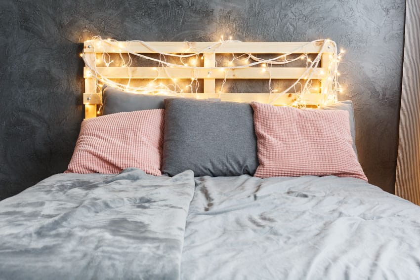 Bedroom with fairy lights, wood headboard, grey and pink pillows and bedding