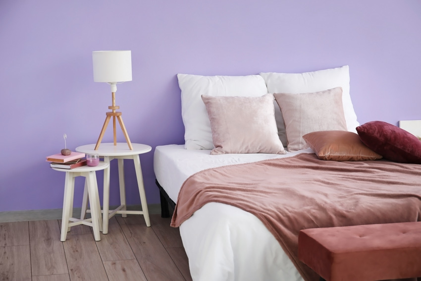 Bedroom with lavender painted wall, pillows, bedding, nightstands, and wood flooring