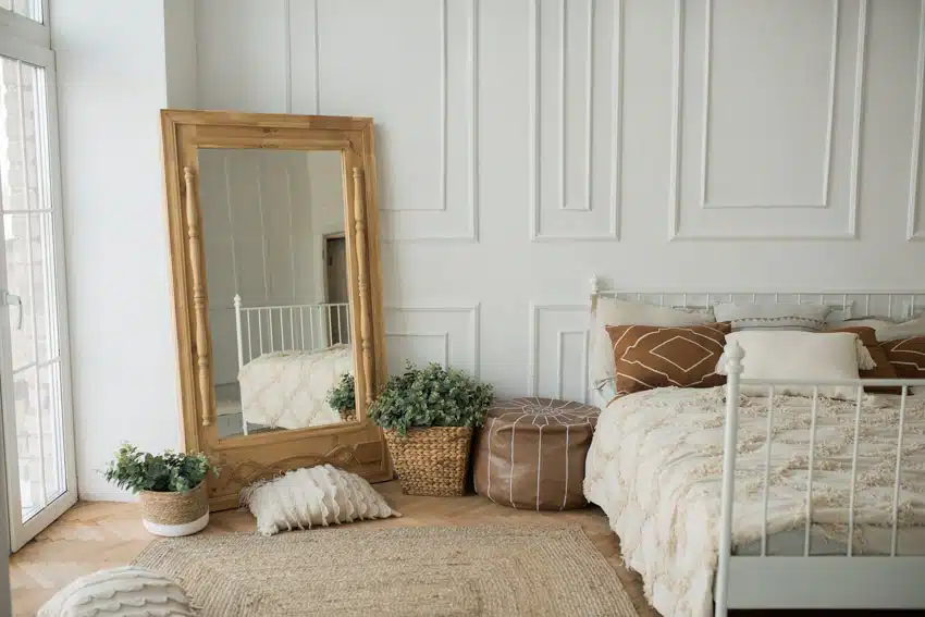 Bedroom with mirror, bed, pillows, paneled wall, rug, wood floor, indoor plants, and window
