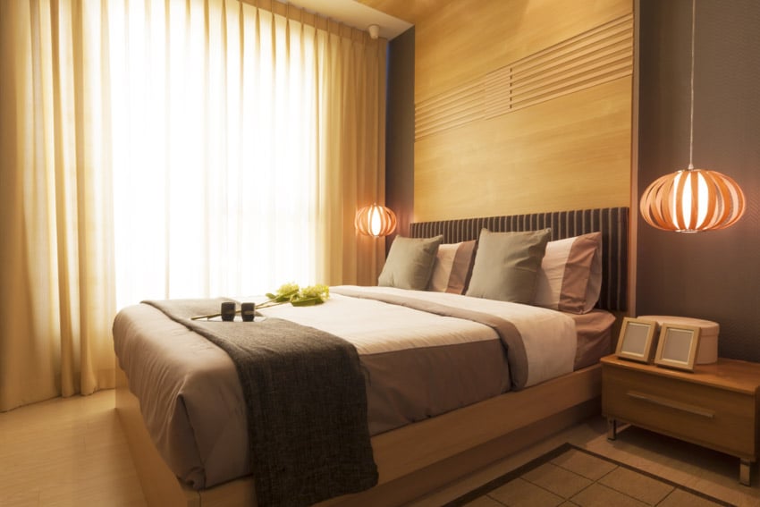 Bedroom with porcelain floor tiles, cream curtains and picture frames on bedside table