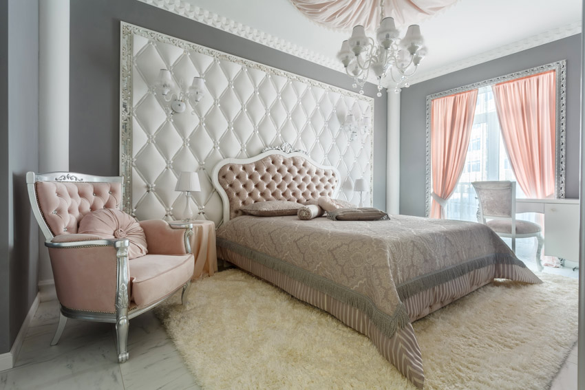 Bedroom with romantic colors, headboard, comforter, chair, rug, chandelier, chair, and window curtains