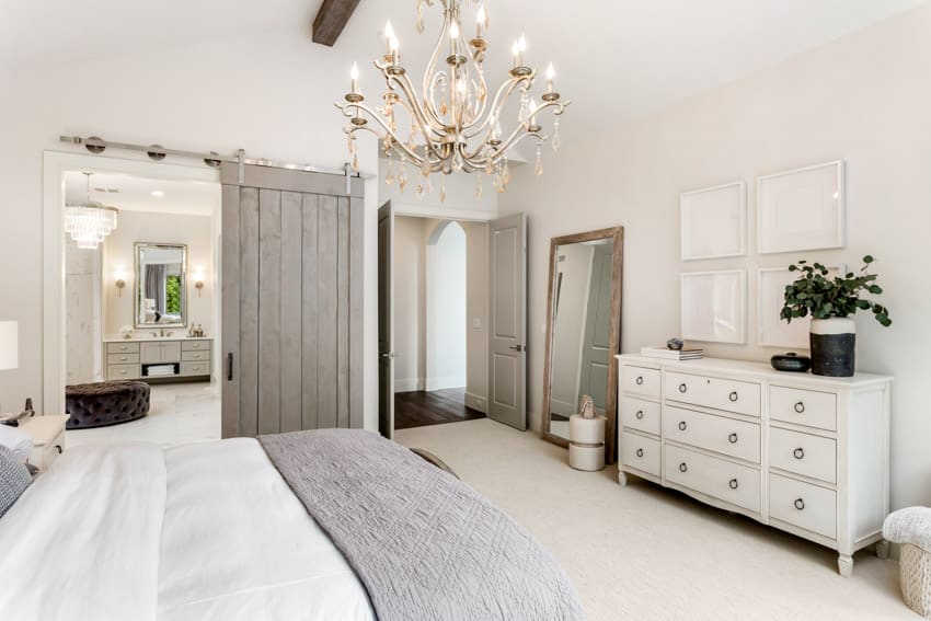 Bedroom with white dresser, table, bedding, chandelier, mirror, and indoor plant