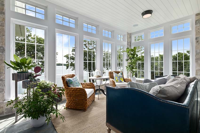 House interior with windows, beadboard ceiling, semi-flush mount light, chairs, couch, pillows, indoor plants, and wood floors