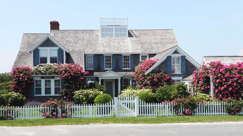 House with blue exterior color, dormer windows, chimney, small fencing and front lawn