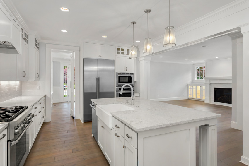 Contemporary kitchen with Bianco Carrara marble countertop, island, sink, faucet, white cabinets, refrigerator, pendant lights, and wood flooring