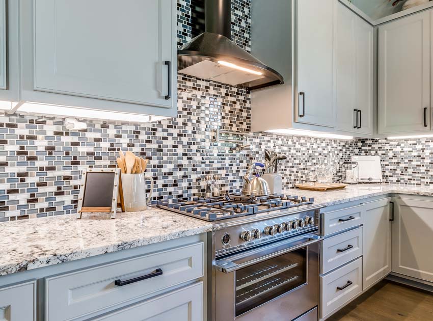 Contemporary kitchen with subway tile mosaic backsplash, shaker style cabinets, range hood, granite countertops, stove, oven, and wood flooring