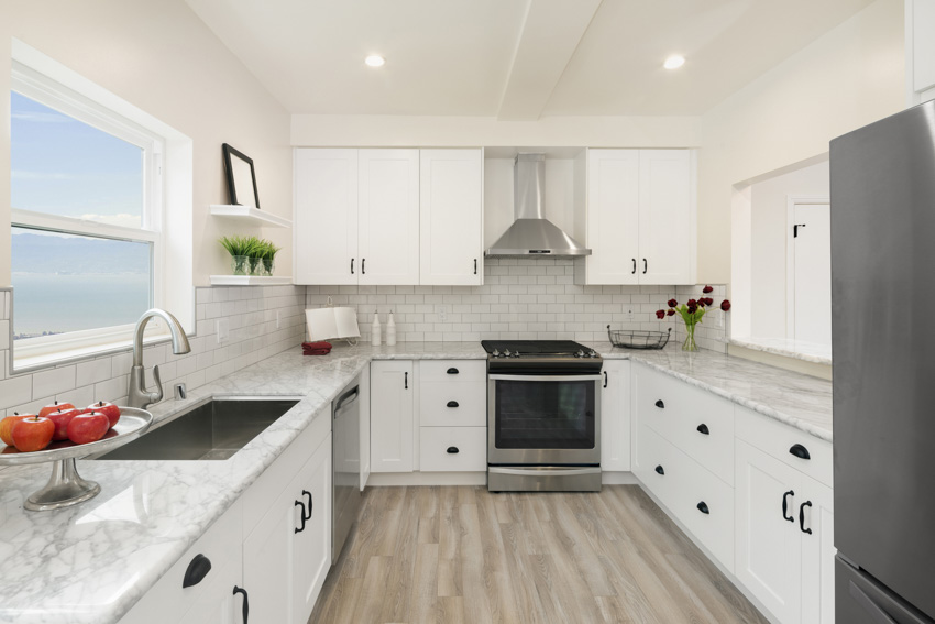 Kitchen with white shaker cabinets, pine floors, steel sink and awning window