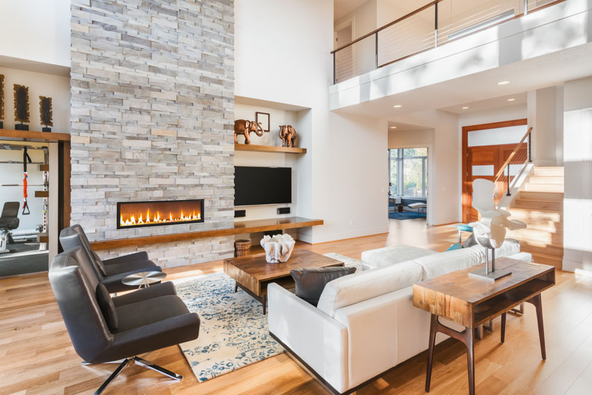 Room with stone wall, black chairs and light grey two-seater with wood console table