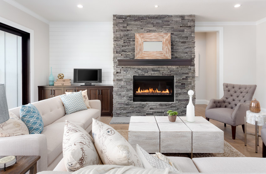 Contemporary living room with stone wall electric fireplace, coffee table, couch, pillows, accent chair, and console table