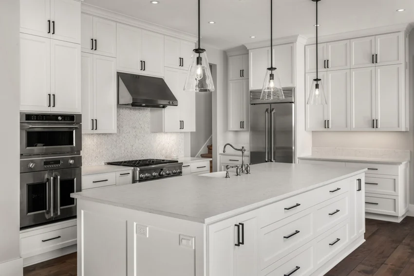 Contemporary white kitchen with cabinets, black hardware, pendant lights, Carrara marble countertop, island, backsplash, range hood, refrigerator, and wood floor