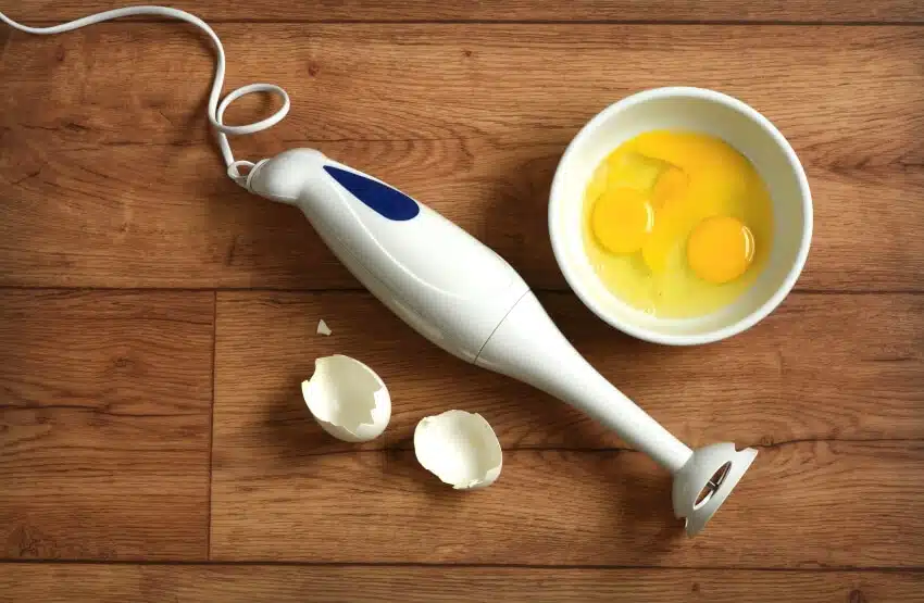 Eggs in bowl and immersion blender on wooden table