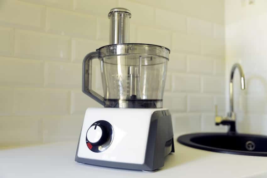 Electric food processor on kitchen countertop with sink on the background