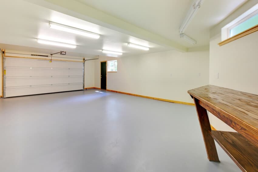 Empty garage with lighting fixtures gray floor and a wooden workspace
