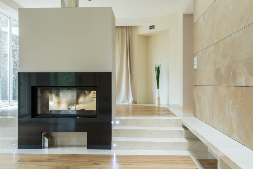 Empty room with fireplace in the middle section of the room, polished wood floors and cream walls