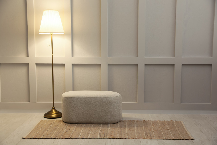 Empty room with paneled wall, floor lamp, oval ottoman, and rug