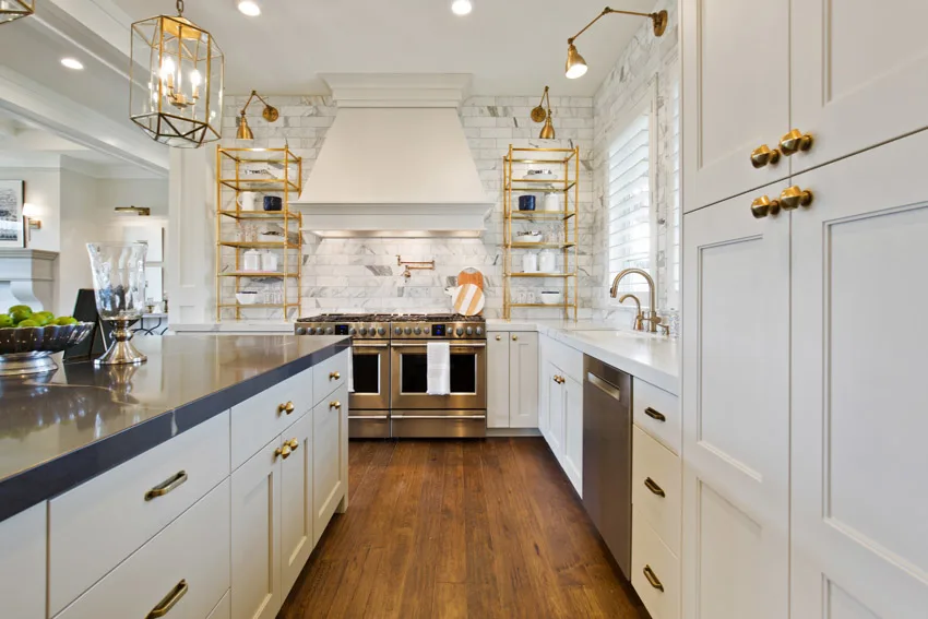 Farmhouse kitchen with Calcatta gold backsplash, white cabinets, wood flooring, countertop, range hood, shelves, and pendant lights