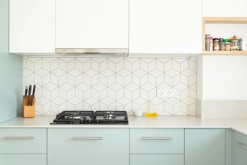 Kitchen with 3D hexagon tile backsplash, countertop, stove, cabinets, and range hood