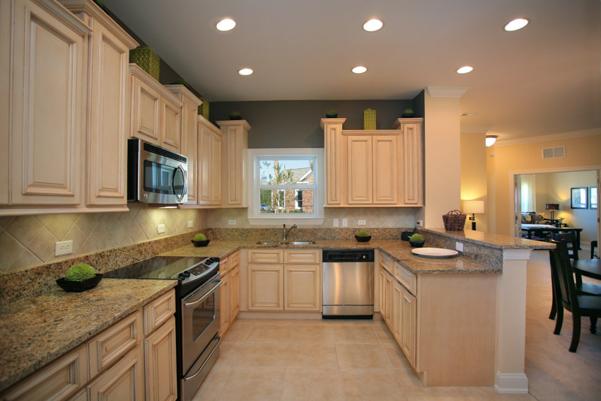 Kitchen with beige countertops, oak cabinets, backsplash, window, oven, and ceiling lights