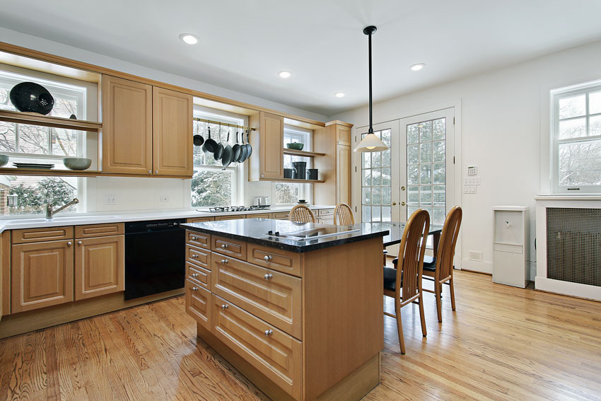 Kitchen with black countertops, island, wood flooring, oak cabinets, chairs, backsplash, and windows