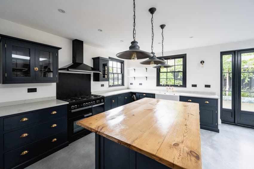 Kitchen with black glass cabinets, wood island, countertops, pendant lights, range hood, stove, and windows