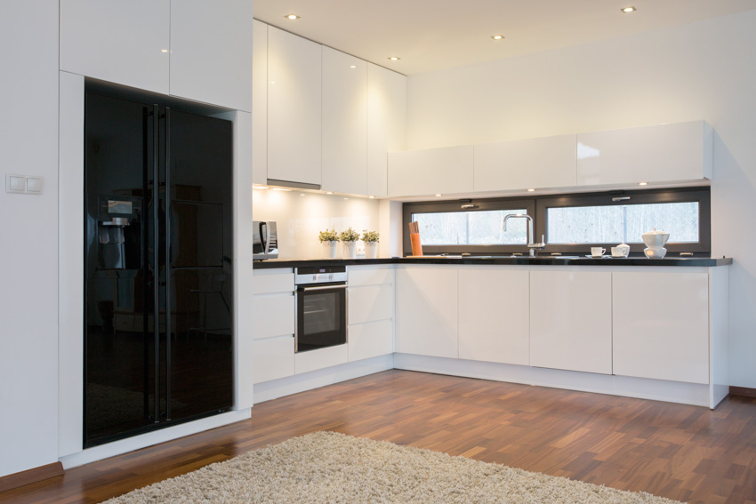 Kitchen with black refrigerator, wood flooring, white cabinets, backsplash, and windows