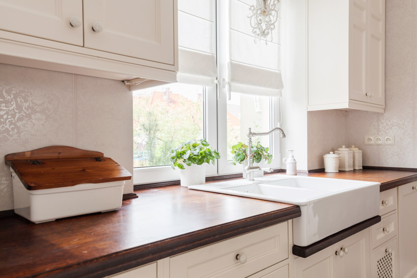 Kitchen with butcher block countertop, sink, windows, cabinets, and backsplash
