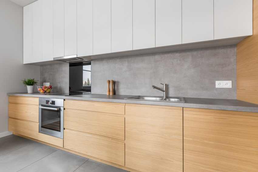 Kitchen with cabinets, backsplash, oven, and concrete countertop 