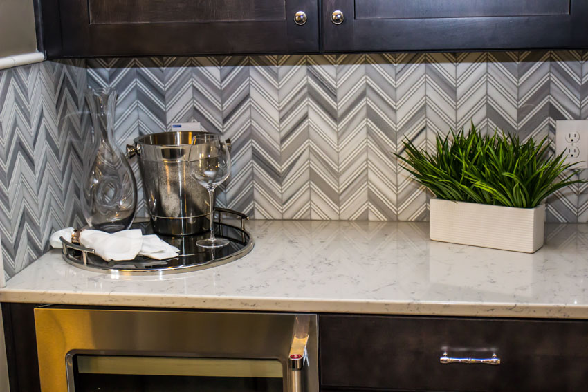 Kitchen with chevron mosaic tile backsplash, marble countertop, indoor plant, and cabinets