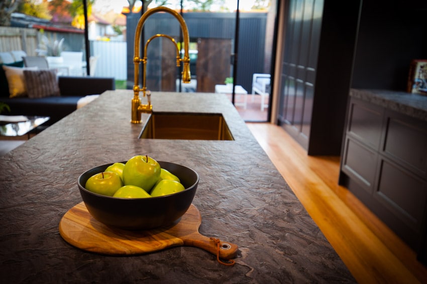 Kitchen with double black quartzite countertop, bowl of fruit, sink, and faucet