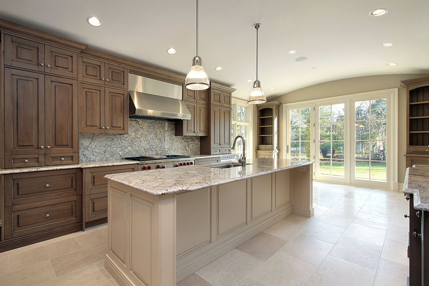 Kitchen with fantasy brown granite countertop, backsplash, tile flooring, wood cabinets, range hood, and pendant lights