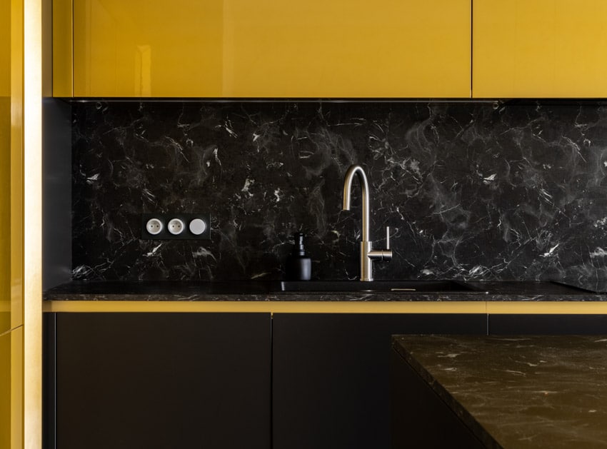 Kitchen with faucet, black diamond quartzite countertop, backsplash, and yellow cabinets