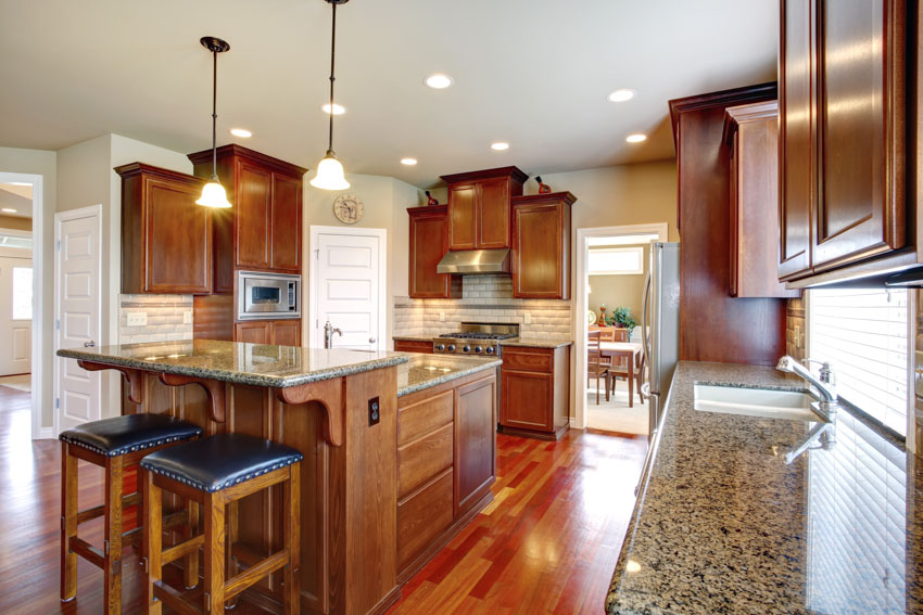 Kitchen with granite countertops, dark oak cabinets, bar stools, pendant lights, backsplash, and wood flooring