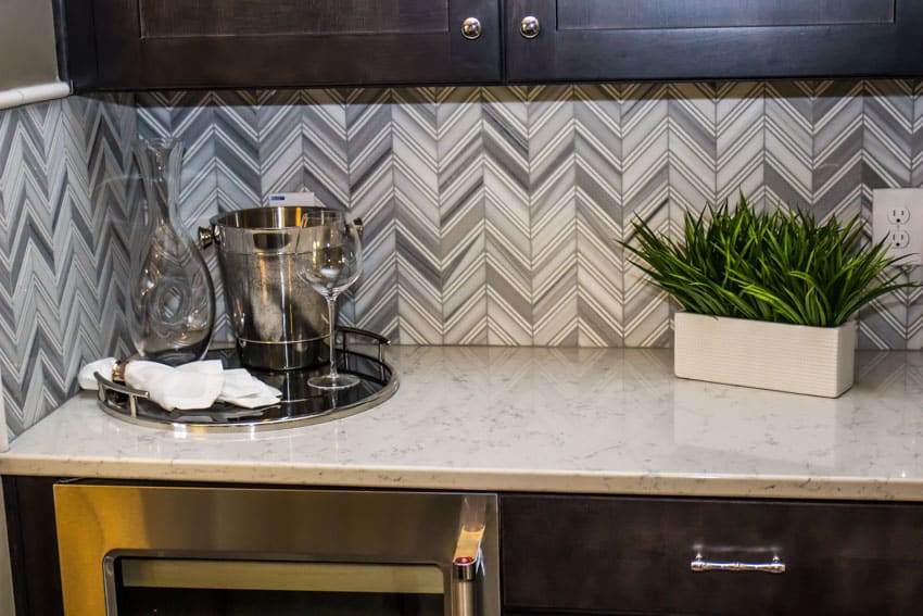 Kitchen with herringbone glass tile backsplash, countertops, wine glass, and plant in a vase