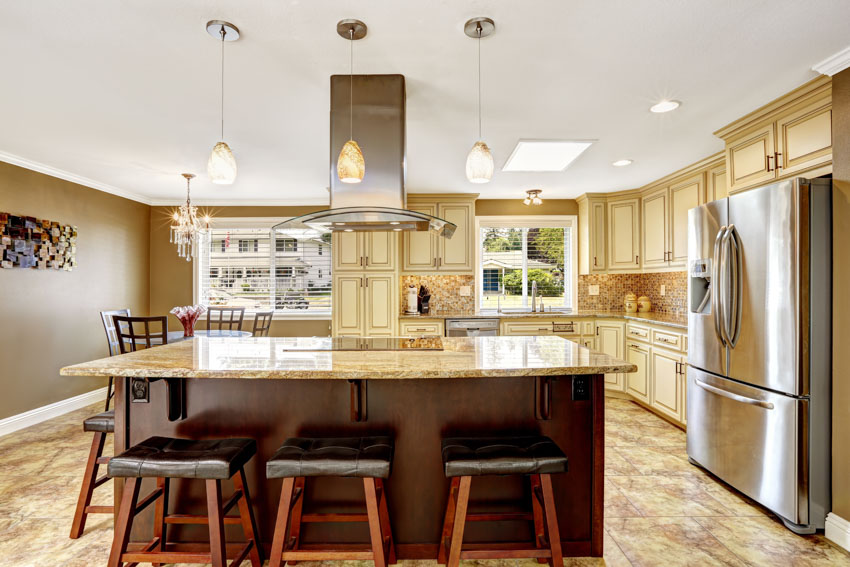 Kitchen with island, bar stools, refrigerator, range hood, windows, cabinets, and fantasy brown granite countertop