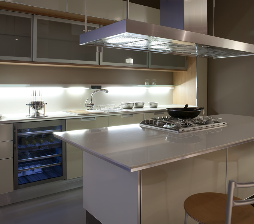 Kitchen with island, stainless steel countertop, wine cooler, range hood, stove, backsplash, and glass cabinets