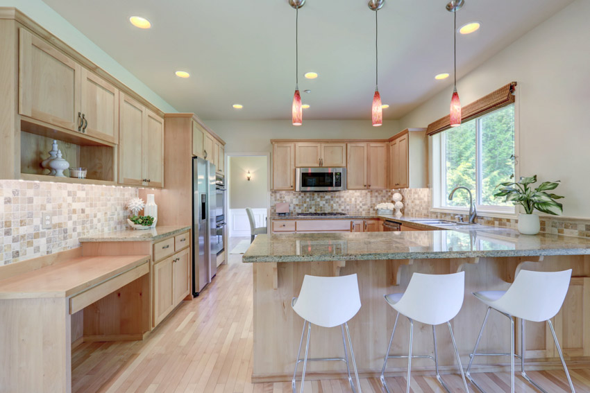 Kitchen with light oak cabinets, countertops, chairs, pendant lights, wood flooring, tile backsplash, and window