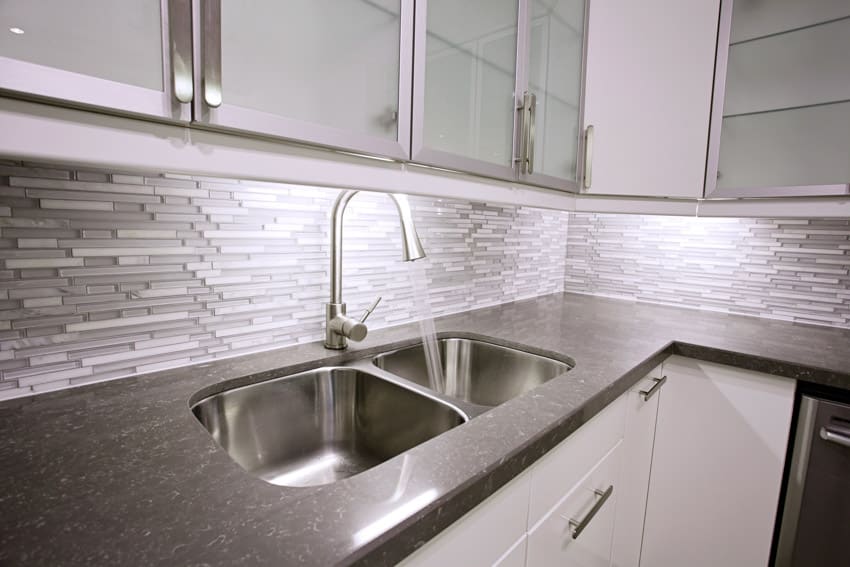 Kitchen with mosaic glass tile backsplash, countertop, sink, faucet, and glass cabinets