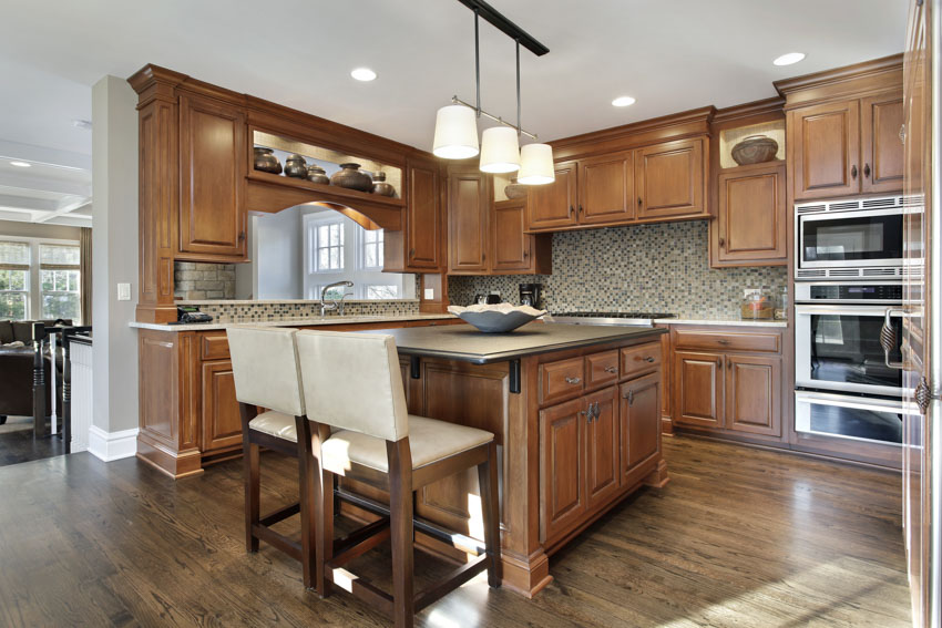 Kitchen with oak cabinets, countertops, backsplash, pendant lights, wood flooring, chairs, oven, and ceiling lights