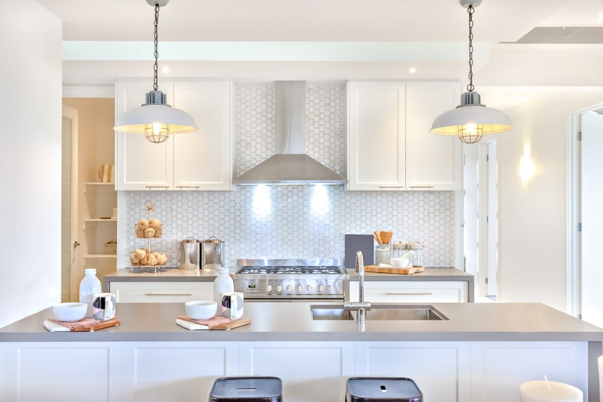 Kitchen with range hood, countertop, island, white cabinets, hexagon tile backsplash, and pendant lights