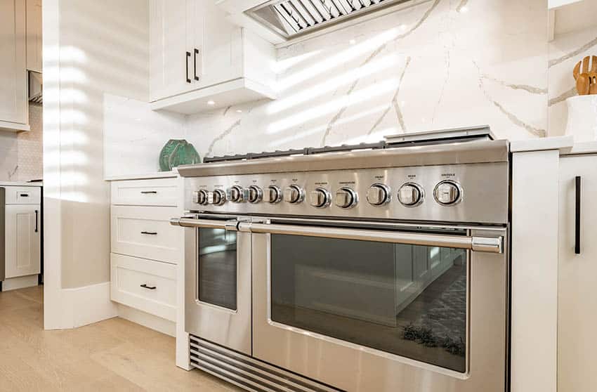 Kitchen with seamless porcelain slab backsplash above stove white cabinets
