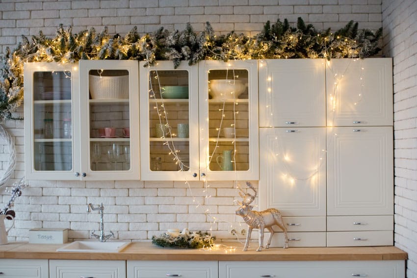 Kitchen with string lights above cabinets, glass doors, white brick backsplash, wood countertop, sink, and faucet
