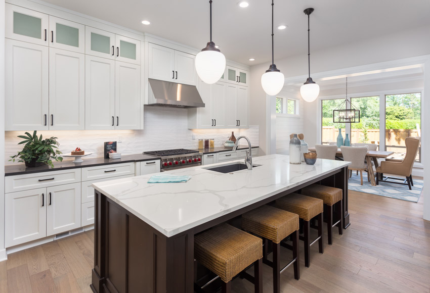 Contemporary kitchen with white cabinets, wood flooring, stools, pendant lights, backsplash, range hood, and quartz countertop for families
