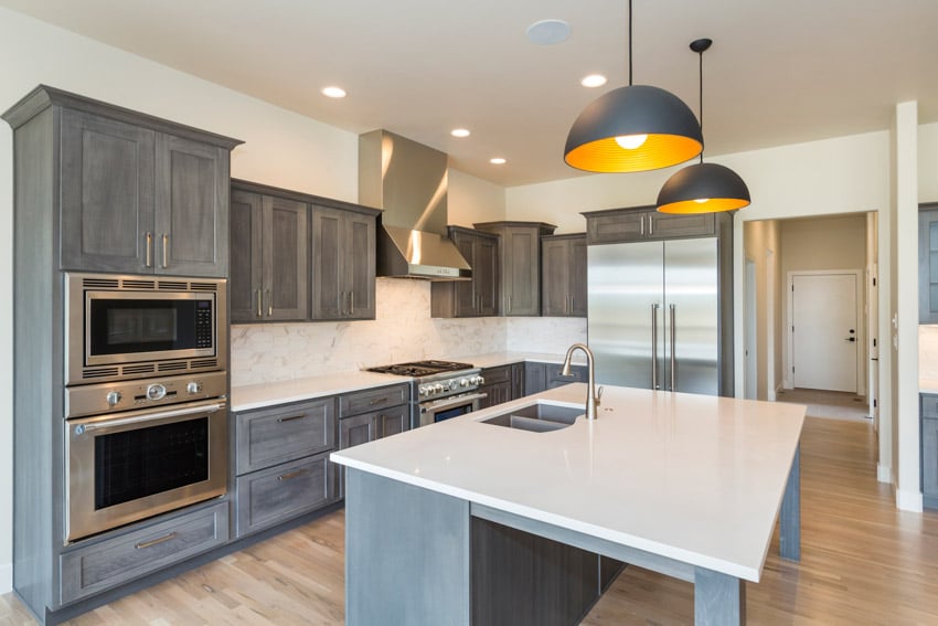 Kitchen with white countertops, pendant lights, gray washed cabinets, oven, backsplash, and range hood