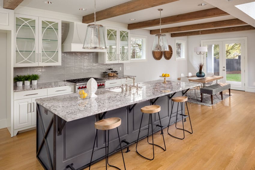 Kitchen with grey island, grey backsplash, exposed beam ceiling and three stools