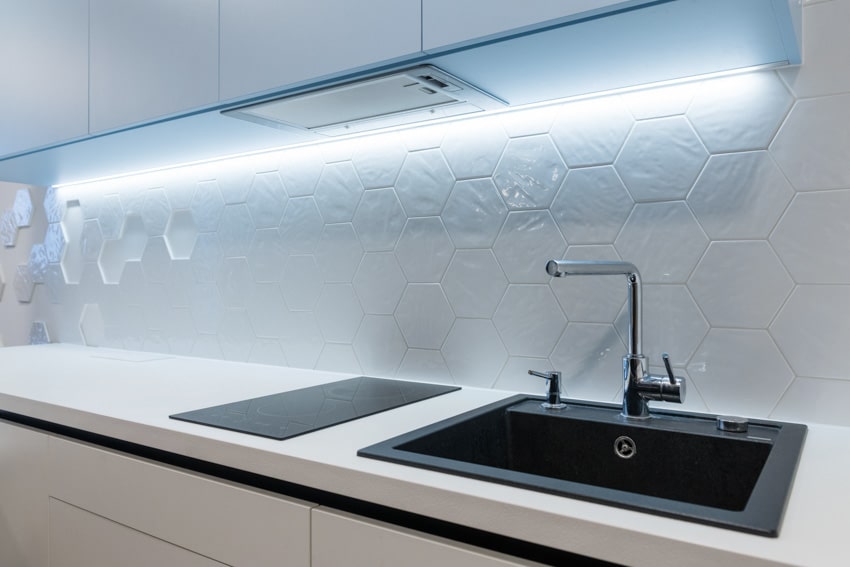 Kitchen with white hexagon tile backsplash, sink, faucet, stove, and cabinets