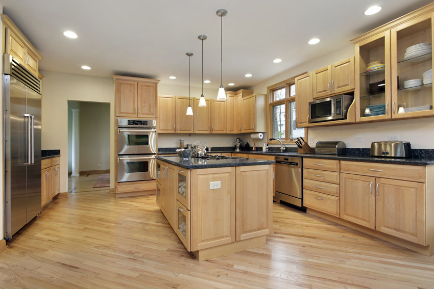 Kitchen with wood flooring, oak cabinets, countertops, island, pendant lights, and window