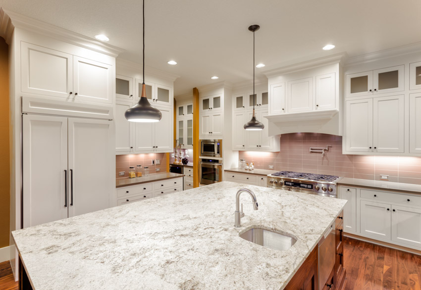 Kitchen with wood floors, island, fantasy brown granite countertop, sink, faucet, cabinets, backsplash, and pendant lights