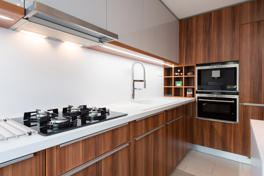 Kitchen with wood veneer cabinets, backsplash, stove, oven, sink, and faucet